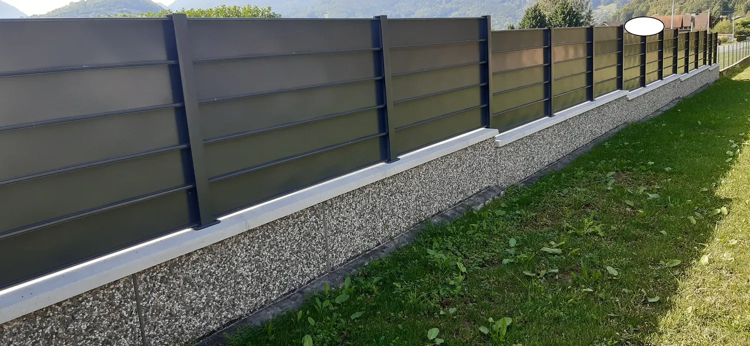 Mur de clôture en Prémurette® gris à faces lisses, le long d’une allée gravillonnée